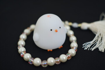 chicken toy with a pearl necklace on a black background close up