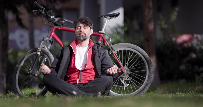 A serene image of a man meditating in a lush park, with a vibrant red bicycle parked next to him as he seeks tranquility.