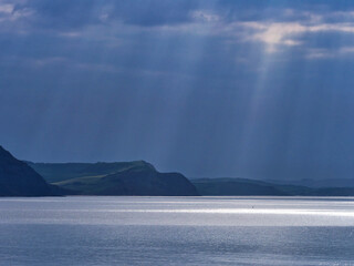 Looking across Lyme Bay towards the jurassic coastline on a spring morning with crepuscular rays shining through dark stormy clouds
