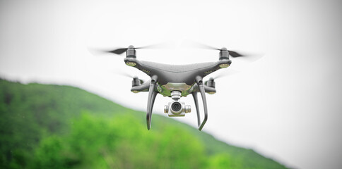 Black flying drone with camera against the background of a forest in the rain.