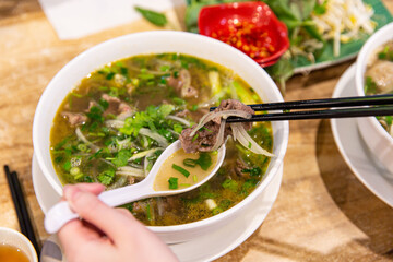 Savoring Pho Bo: A Lively Scene of Enjoying Traditional Vietnamese Beef Noodle Soup with Fresh Herbs