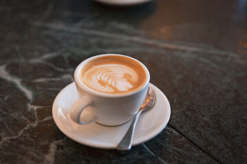Elegant Cappuccino with Leaf Pattern Latte Art in White Ceramic Cup, Set on a Marble Cafe Table