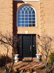 black entrance door in a brick house with facade and window.