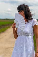woman is holding a white fan in her hand while walking on a dirt road