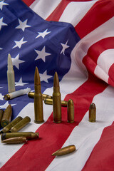 Closeup of cartridges and bullets of different sizes arranged on top of American flag with stars and stripes