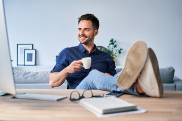Relaxed businessman having break drinking coffee sitting with feet up on the desk looking at...