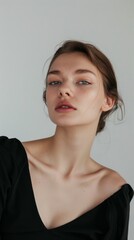 Elegant portrait of a woman in a black off-shoulder dress, showcasing a minimalist makeup look, set against a simple backdrop for a timeless feel.