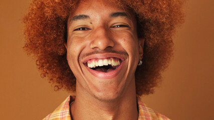 Close up, portrait of a laughing stylish curly guy, looking at the camera, isolated on brown...