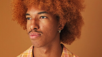 Close up, portrait of a stylish curly guy turning his head, isolated on brown background in the...