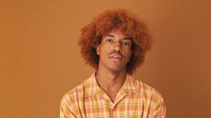 Close up, stylish curly guy looking at the camera listens and strongly disagrees, isolated on brown background in the studio