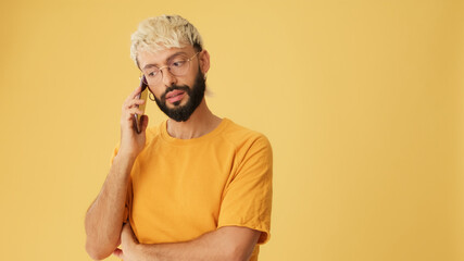 Guy with glasses, dressed in yellow T-shirt, talking on mobile phone, isolated on yellow background...