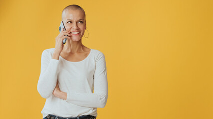 Smiling young hairless woman talking on mobile phone, advertising space, isolated on yellow...