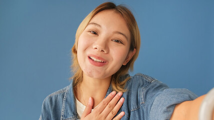 Close-up of young woman looking at camera making video call, welcome sign, isolated on blue...