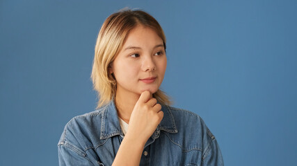 Close-up of young woman dressed in denim shirt thinking something, having good idea, isolated on...