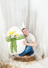 Funny man with rabbit ears sitting in the nest Easter holiday concept and holding egg