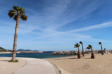 Plages de sable artificielles du Mourillon à Toulon, dans le Var, anse des Pins, avec un paysage de plage déserte et des palmiers, sous un ciel bleu, au bord de la mer Méditerranée (France)