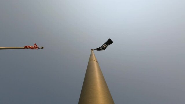 Prisoner of War Flag and American Flag. Metal flagpole with Prisoner of War (POW) flag waving against a clear sky. Next to it, the American Flag also waves.