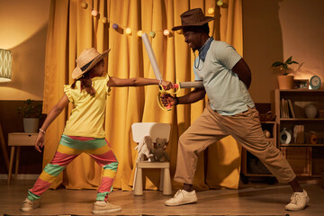 Portrait of smiling Black little girl in sword fight with father while acting on stage in makeshift...