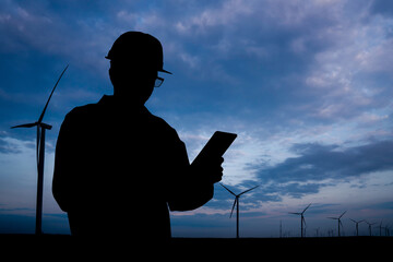 Silhouette of engineer with tablet computer and wind turbines at sunset.