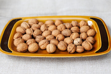 walnuts in shell on a brown ceramic plate on a gray background close-up