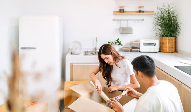 couple storing kitchen tools new house together. lover unpack box decorating new home kitchen support each other. wife and husband picking tools in the box relocating to new living location kitchen