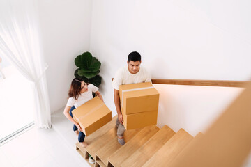 lover lifting box walking up stairs in new home. family together carrying cardboard box up next level of house. wife and husband help holding packaging box next floor relocating preparing new house