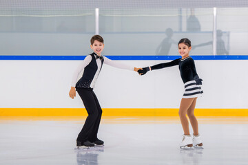 A boy and girl ice skaters are performing a routine on the ice.