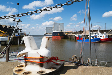 Large ship for transporting aggregates in Whitstable harbour. There is a large mooring bollard in the foreground in softer focus.