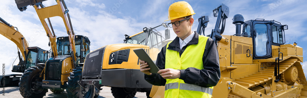 Poster Engineer in a helmet with a digital tablet on the background of construction machines