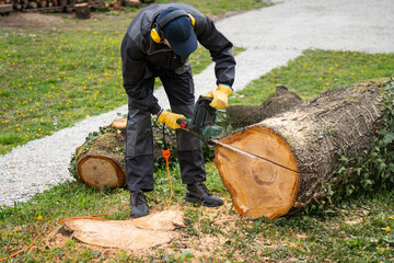A man in uniform cuts an old tree in the yard with an electric saw.