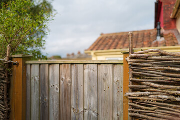 Shallow focus of a natural weave wattle fence seen at the back of holiday cottages on the east coast of England. The terraced back gardens are part of holiday lets on the east coast of England. - obrazy, fototapety, plakaty