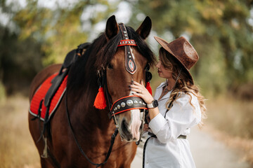 Obraz premium A girl in a white shirt and hat stands next to the horse.