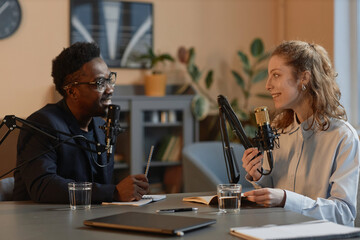 Side view of smiling African American male host discussing politics with young Caucasian female...