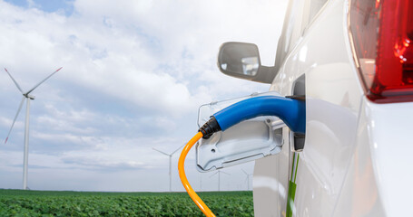 Electric car with charging plug on a background of wind turbines..