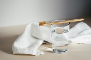 Glass with drinking water under bamboo toothbrush with soft fiber for sensitive gums and teeth