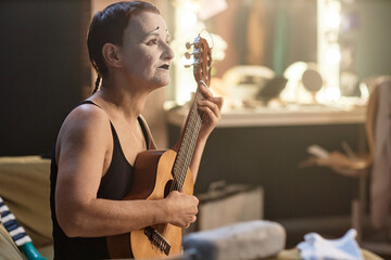 Side view portrait of female mime performer playing ukulele while rehearsing backstage, copy space