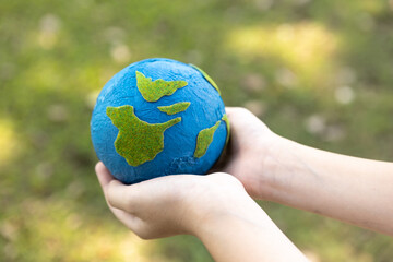 Young boy's hand holding planet Earth globe at natural park background as Earth day to save this...