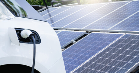 Close up of electric car with a connected charging cable on the background of solar panels..