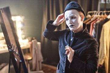 Waist up portrait of female mime performer dressing in costume and looking in mirror backstage...