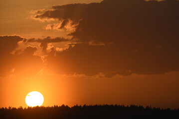 Colorful sunset in the evening. The setting disk of the sun over the forest. Clouds and a yellow...