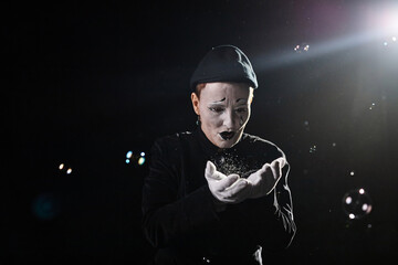 Minimal portrait of mime artist playing with soap bubbles and catching against black background,...
