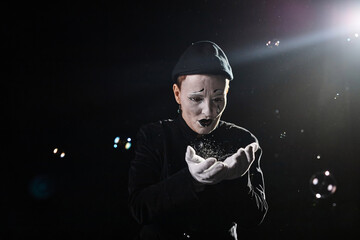 Minimal portrait of mime artist playing with soap bubbles and catching against black background, copy space