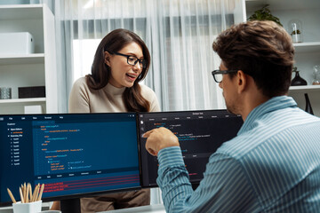 Woman colleague standing opposite to man programmer working on desk to discuss coding website...