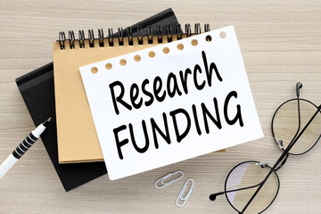three notepads on a work desk. text on a page RESEARCH FUNDING