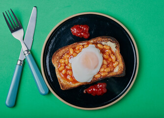 Beans on toast with a poached egg on top with tomato sauce,on a green background.