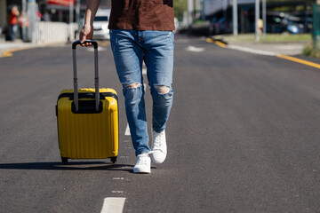 man wearing casual clothes walking to the airport with his yellow suitcase