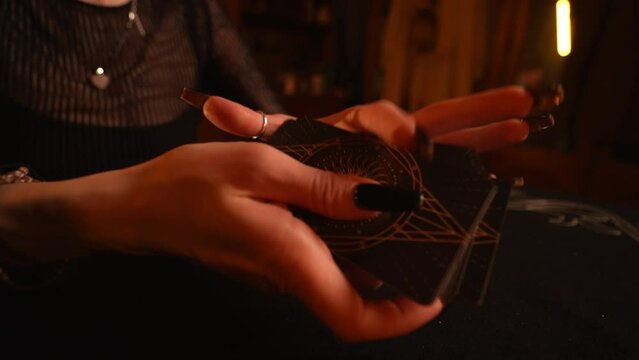 Closeup hands of female fortune-teller shuffling deck of tarot cards by light of burning candles. Otherworldly clairvoyant performing esoteric rite, forecasting fate. Concept of divination, magic.