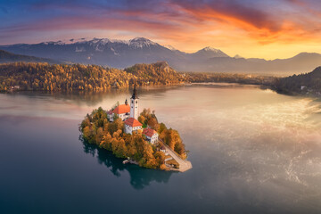 Aerial view of a colourful autumn sunrise over Lake Bled with snow-capped Julian Alps and Bled...