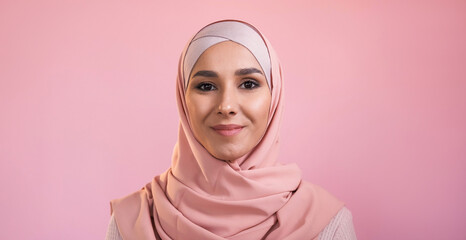 Islamic woman portrait. Muslim beauty. Happy confident smiling pretty female face in hijab headscarf isolated on pink empty space background.