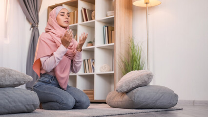 Praying muslim. Islam religion. Allah worship. Faithful woman in hijab reading Holy Quran on floor at light modern home interior with free space.